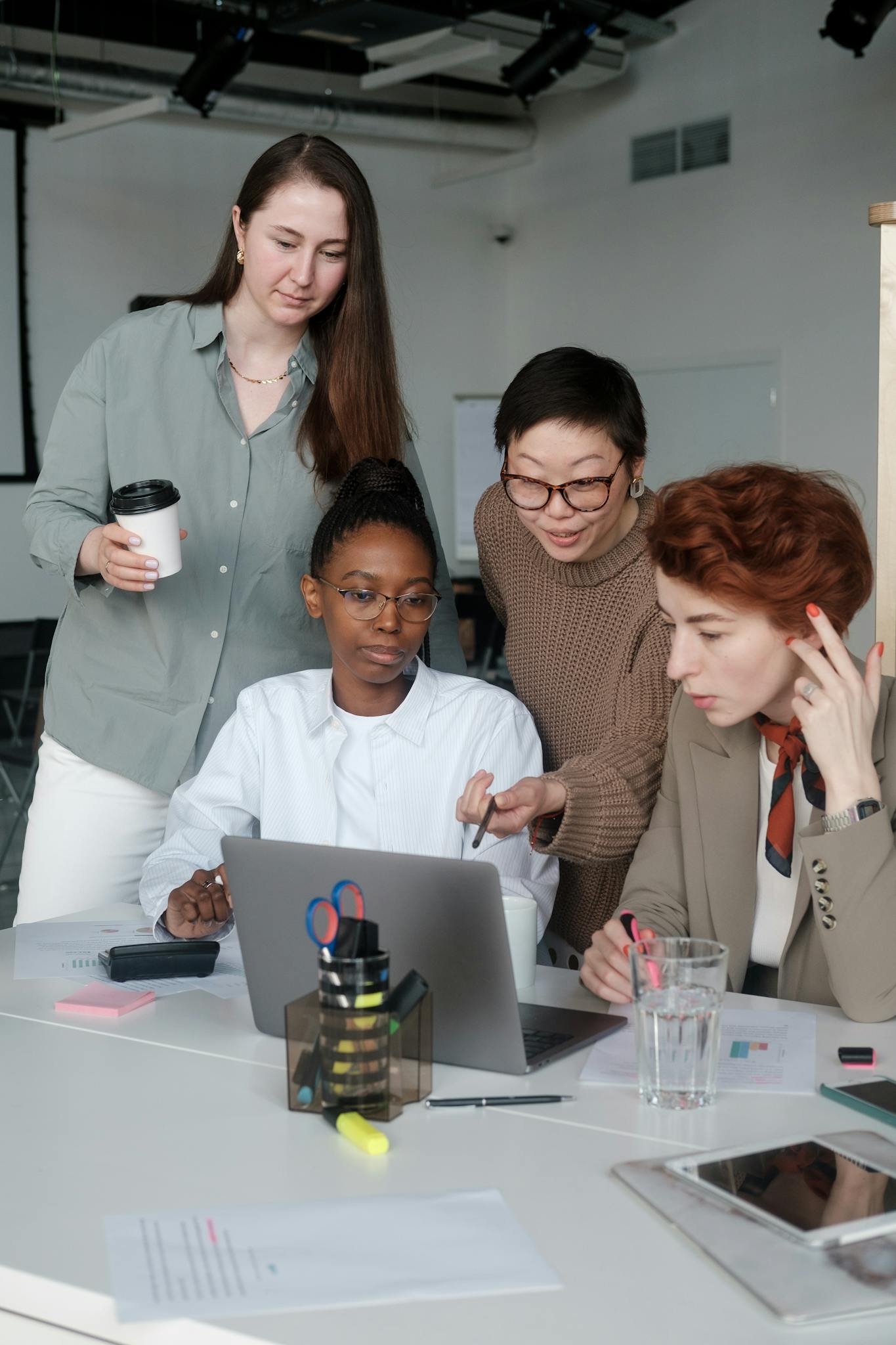 A diverse group of women working together at a laptop in an office setting.